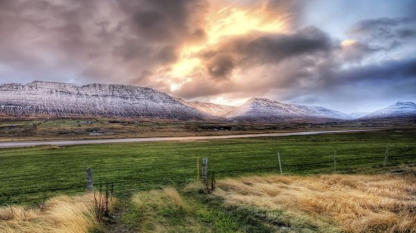 click to free download the wallpaper--Great Scene of Nature - The Dark Sky with Thick Clouds, Snow-Capped Mountains, Green Grass, What a Contrast!