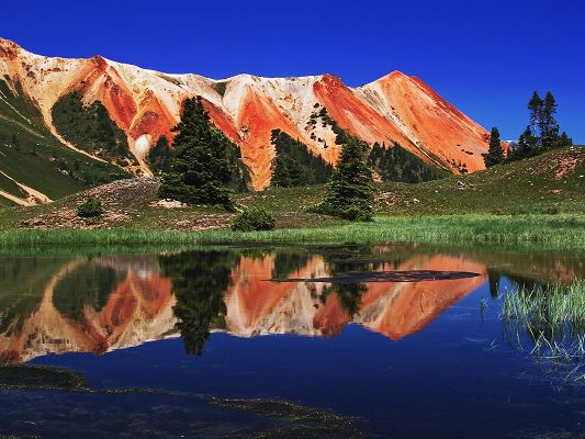 click to free download the wallpaper--Nature Landscape Image, Red Mountains Along the Blue Sea, Green Trees in the Stand